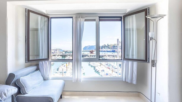 A room with a large bay window, a white sofa, and a floor lamp. - Old Port, Apartamento con Vistas al Puerto (Bermeo)
