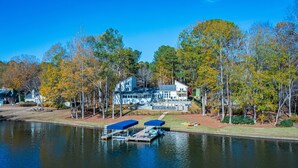 A lakeside property with a large house, dock with boats, and surrounding trees.