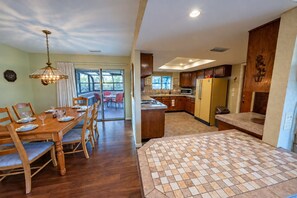 A dining area with a wooden table and chairs, a kitchen with wooden cabinets and a yellow refrigerator, and a view through a glass door to an outdoor patio.