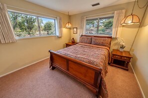 Un dormitorio con una cama de madera, dos mesitas de noche, una lámpara de pie y una ventana con cortinas, además de una lámpara colgante.