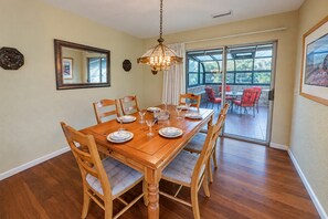 Comedor con mesa de madera dispuesta para cuatro personas, sillas, una lámpara de araña y un ventanal con vistas.