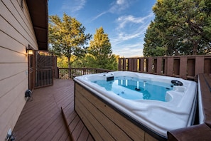 Ein Whirlpool auf einer Holzterrasse mit Blick auf Bäume und einen klaren Himmel.