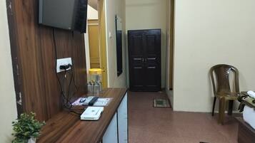 A hallway with a wooden desk, a television mounted on the wall, a black door, and a plastic chair.