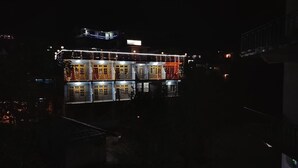 A multi-story building with balconies, illuminated by string lights. - Ishwar Guest House (Dharamshala)