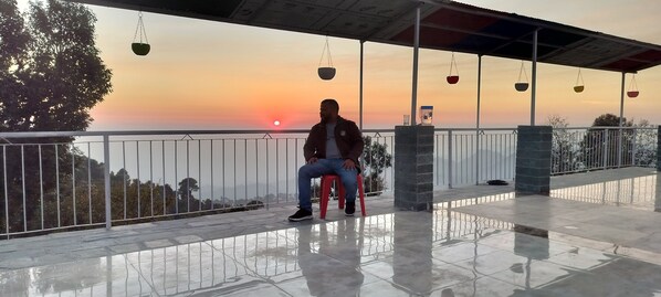 Una persona sentada en una silla roja en un balcón con vista al atardecer.