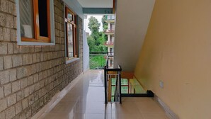 A corridor with tiled flooring, a staircase, and a view of a green balcony with railings. - Ishwar Guest House (Dharamshala)
