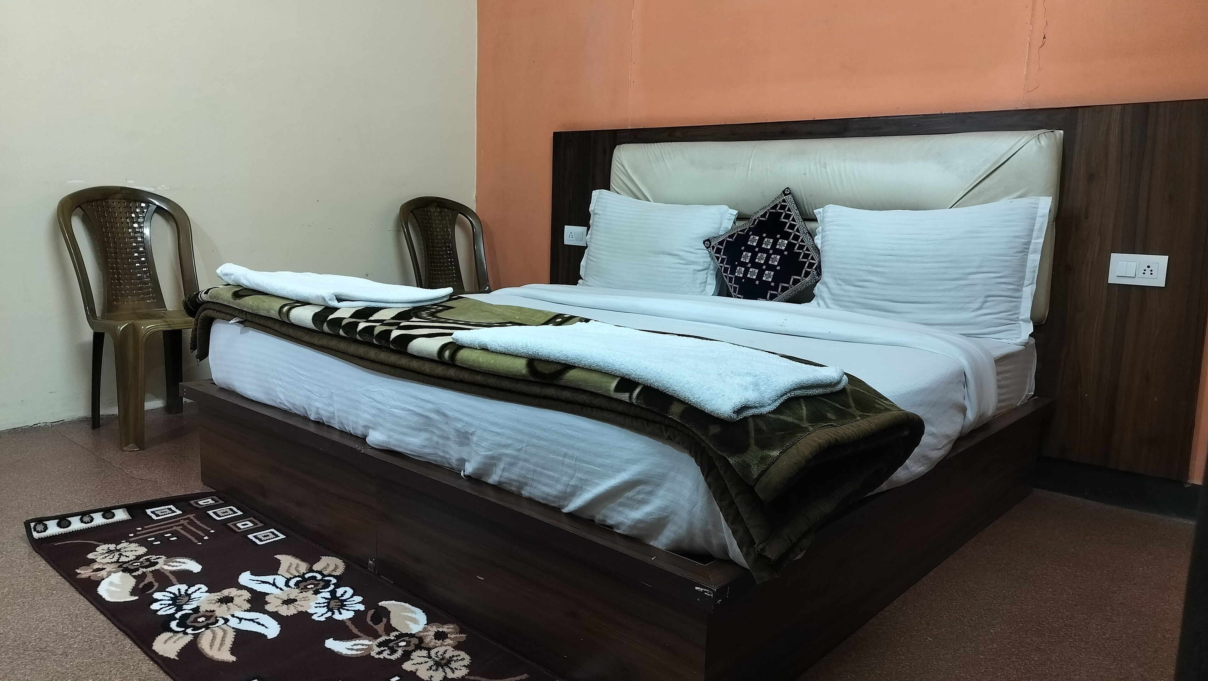 A neatly made bed with a patterned blanket, two pillows, and a floral rug.