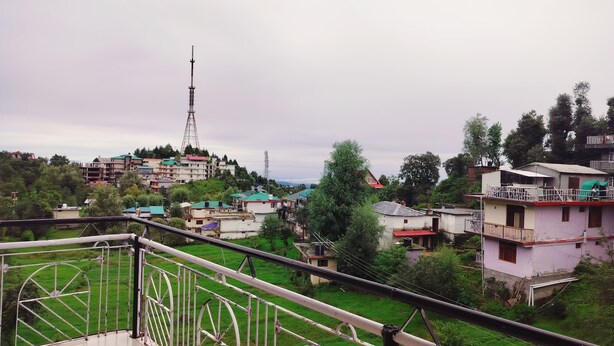 A residential area with houses, a prominent communication tower, and lush greenery. - Ishwar Guest House (Dharamshala)