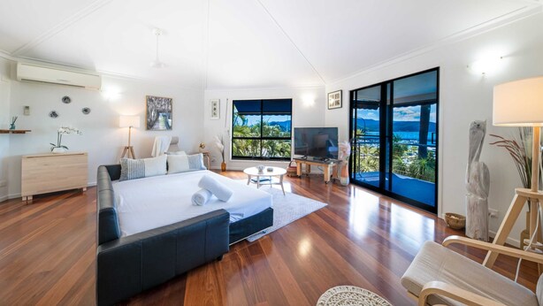 A modern bedroom with a large bed, a TV, and a view of the ocean.