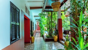 A corridor with tiled flooring, potted plants, and a view of a pool. - RESIDENCE 1960 (Siem Reap)