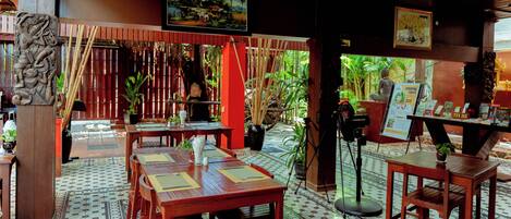 Un restaurant avec des tables et des chaises en bois, un comptoir d’information touristique et diverses plantes.
