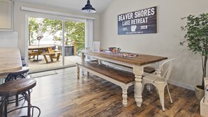 A dining area with a wooden table and bench, a pendant light, and a sign on the wall advertising a lake retreat. - Lakefront Luxury! Direct Water Access, Spa, Fire Pit & Boat Launch-Sleeps 17 (Rogers)