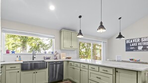 A modern kitchen with light green cabinets, a stainless steel sink, and a wooden floor. - Lakefront Luxury! Direct Water Access, Spa, Fire Pit & Boat Launch-Sleeps 17 (Rogers)