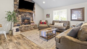 A living room with a stone fireplace, leather sofas, a coffee table, and a television mounted on the wall. - Lakefront Luxury! Direct Water Access, Spa, Fire Pit & Boat Launch-Sleeps 17 (Rogers)