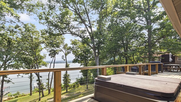 A wooden deck with a view of a lake, surrounded by trees. - Lakefront Luxury! Direct Water Access, Spa, Fire Pit & Boat Launch-Sleeps 17 (Rogers)
