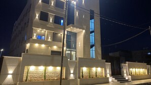 A modern building with multiple floors, illuminated windows, and a well-lit entrance area with steps leading up to the door. - Royal Group Hotel Irbid (Irbid)