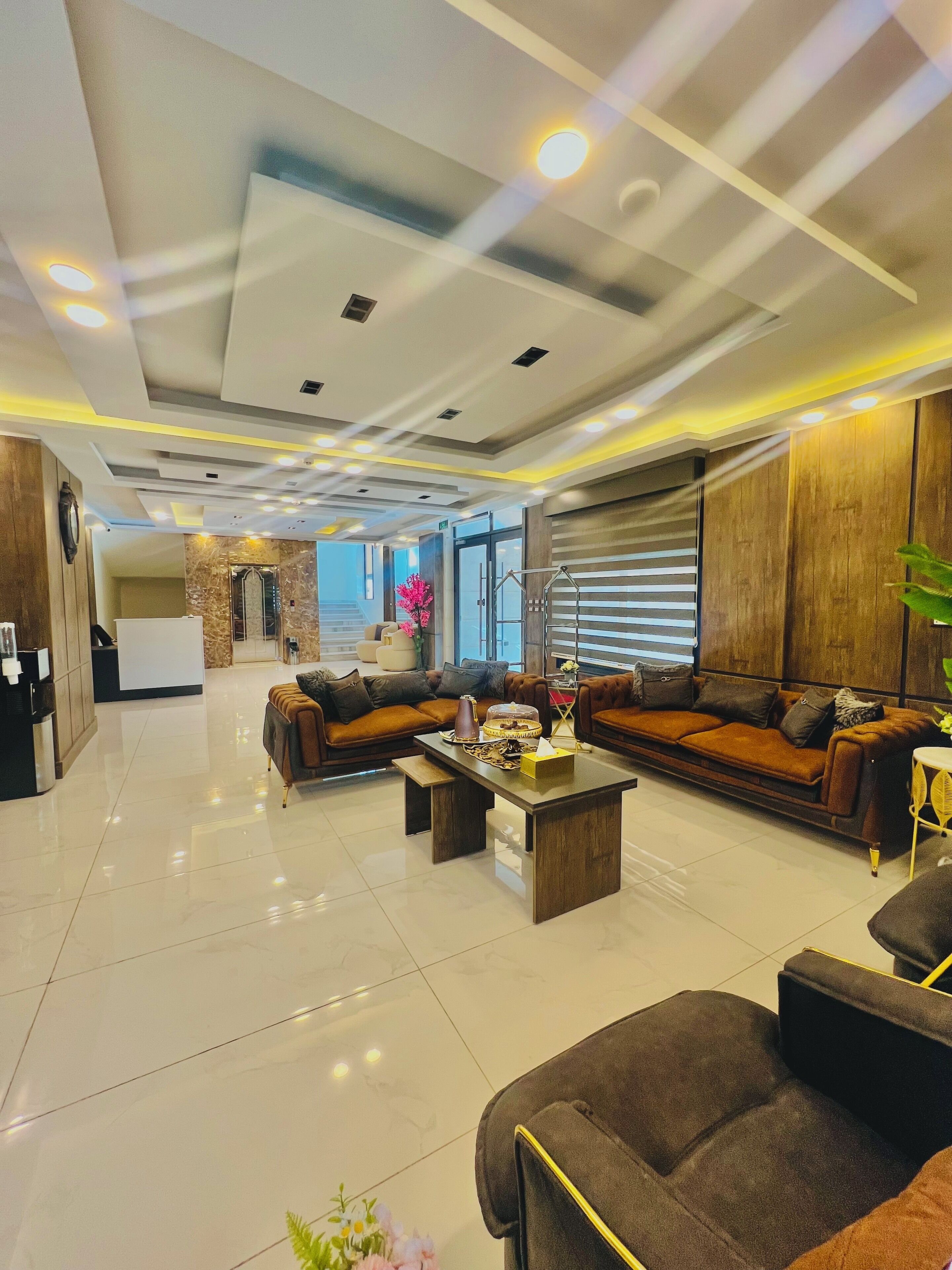 A modern hotel lobby with a sofa set, a coffee table, and a reception area in the background.