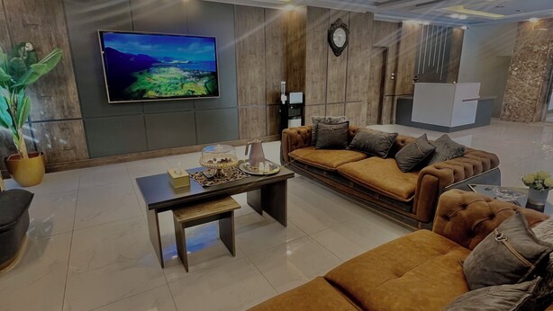 A modern living room with a large flat-screen TV, a sofa set, a coffee table, and a decorative plant. - Royal Group Hotel Irbid (Irbid)