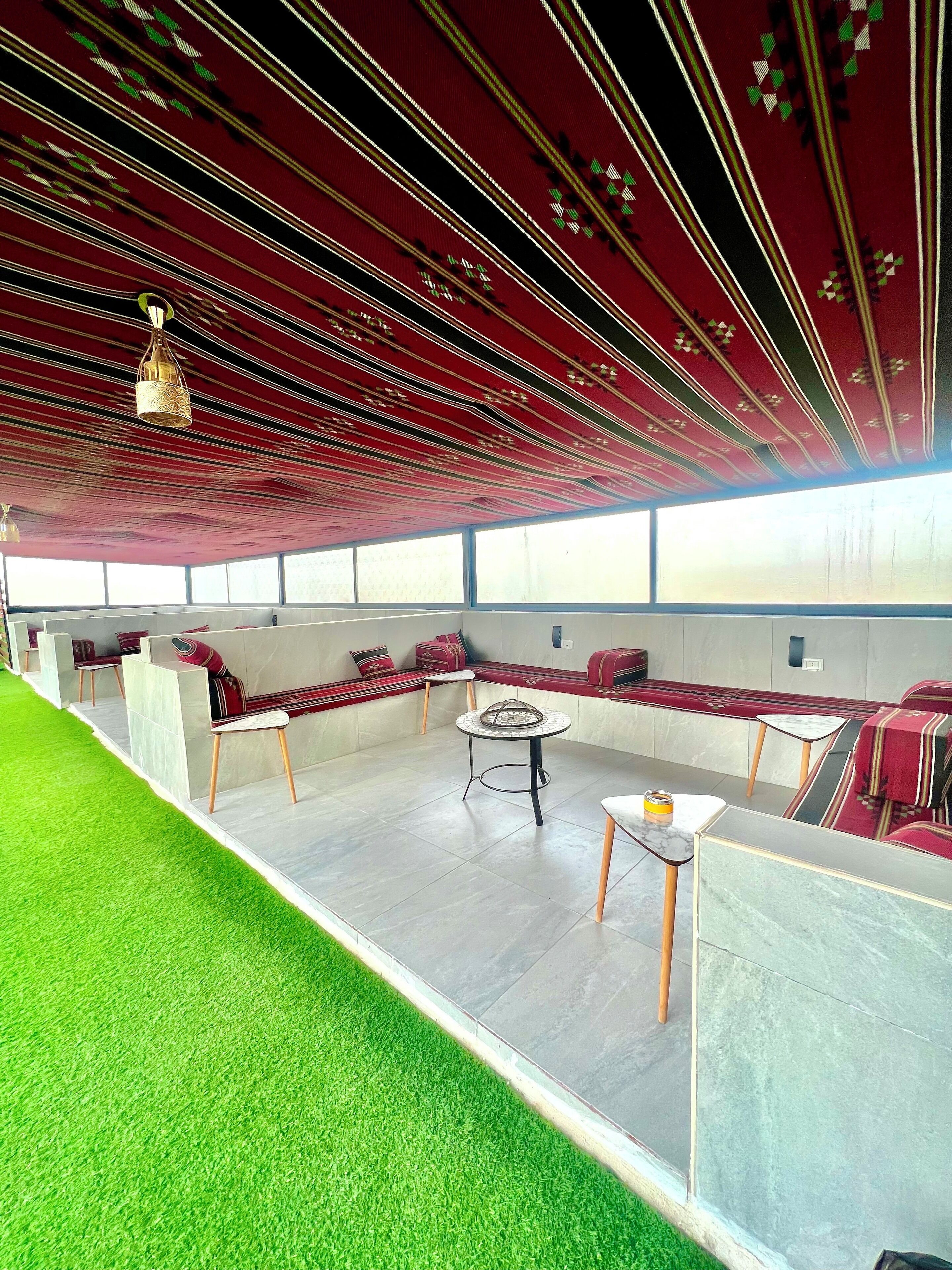 A spacious indoor area with a high ceiling, red patterned ceiling, and a seating area with red upholstered benches and a round table.