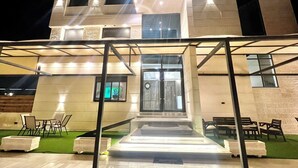 A modern building with a well-lit entrance, outdoor seating, and a visible logo on the facade. - Royal Group Hotel Irbid (Irbid)