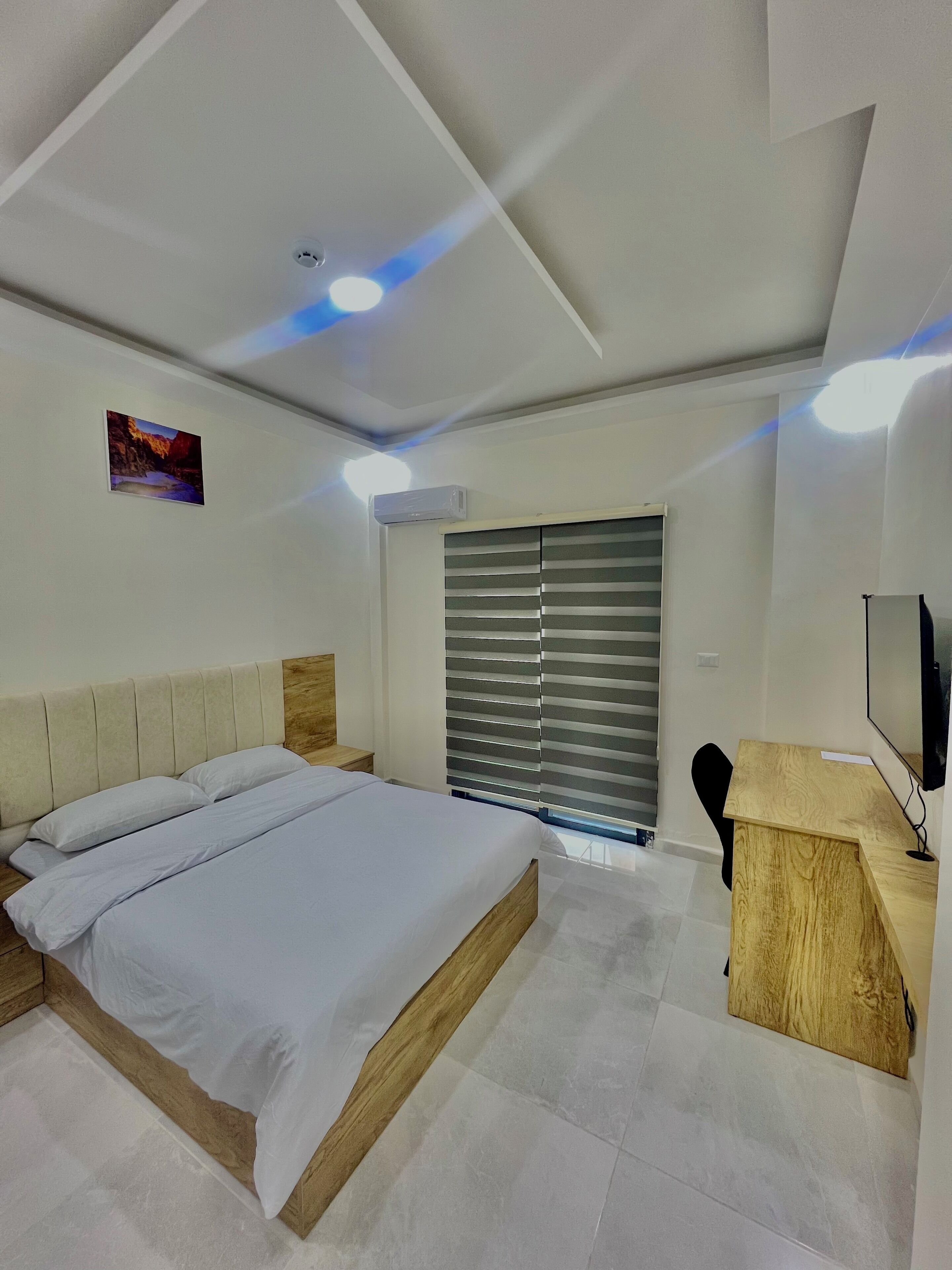 A modern bedroom with a bed, a desk, and a TV.