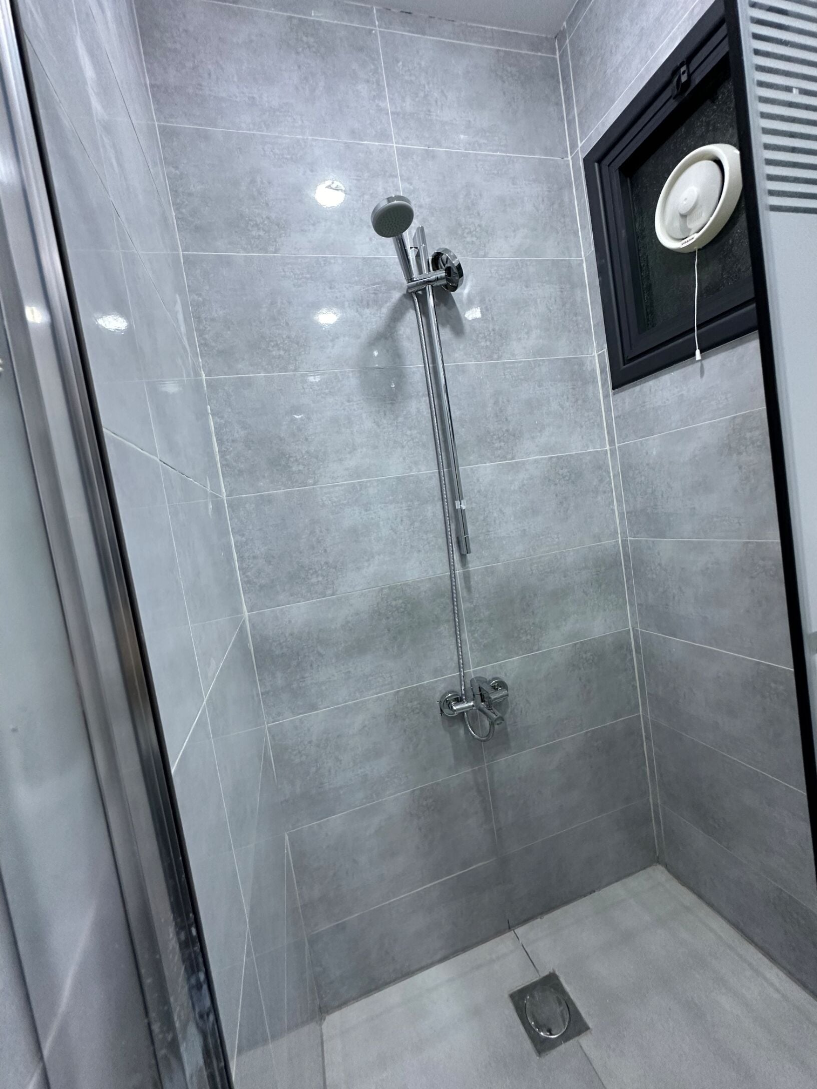 A modern shower with a handheld showerhead and a wall-mounted faucet.