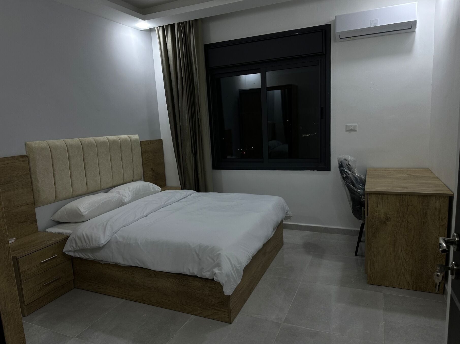 A bedroom with a wooden bed, a nightstand, a wooden cabinet, and a window with curtains.