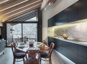 A modern kitchen with dark cabinetry, a wooden dining table set for four, and a view of a snowy landscape through large windows.