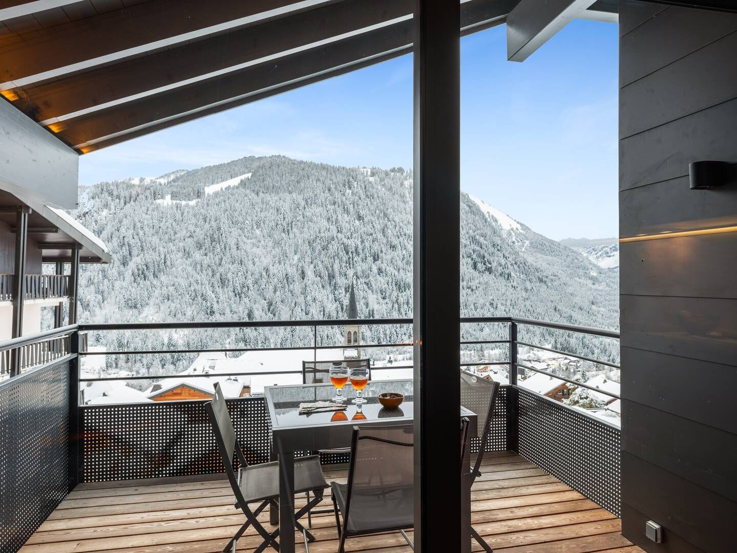 Ein Balkon mit Holzboden, Tisch und Stühlen sowie Blick auf schneebedeckte Berge.