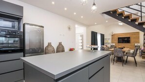 Une cuisine moderne dotée d’un îlot central, de fours encastrés et d’un coin repas avec un escalier.