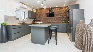 Une cuisine moderne dotée d’un îlot central, de meubles de couleur grise, d’un mur d’accent en briques et d’un réfrigérateur en acier inoxydable.