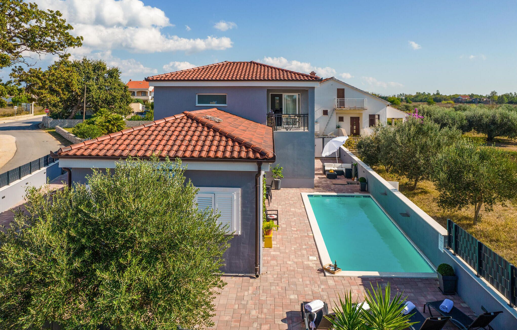 Una casa de dos pisos con piscina, un porche cubierto y vistas a olivos.