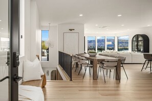 A modern interior with a dining area, a sofa set, and large windows offering a mountain view.