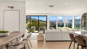 A modern living room with a large sofa, dining area, and a view of mountains through large windows.