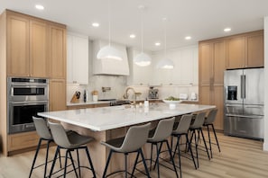 Eine moderne Küche mit Holzausstattung, Edelstahlgeräten, einer großen Kochinsel mit Barhocker und Pendelleuchten.
