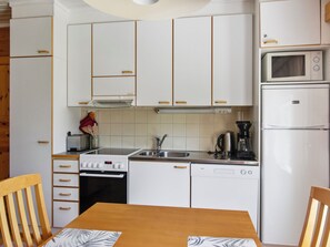 A compact kitchen with white cabinets, a stove, a sink, a coffee maker, and a refrigerator. - Urupää b 6 by Interhome (Inari)