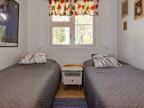 A bedroom with two single beds, a nightstand, a window with curtains, and a wall-mounted picture. - Urupää b 6 by Interhome (Inari)