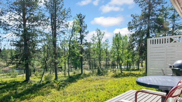A wooden deck with a table and chairs, overlooking a forested area with a lake. - Urupää b 6 by Interhome (Inari)
