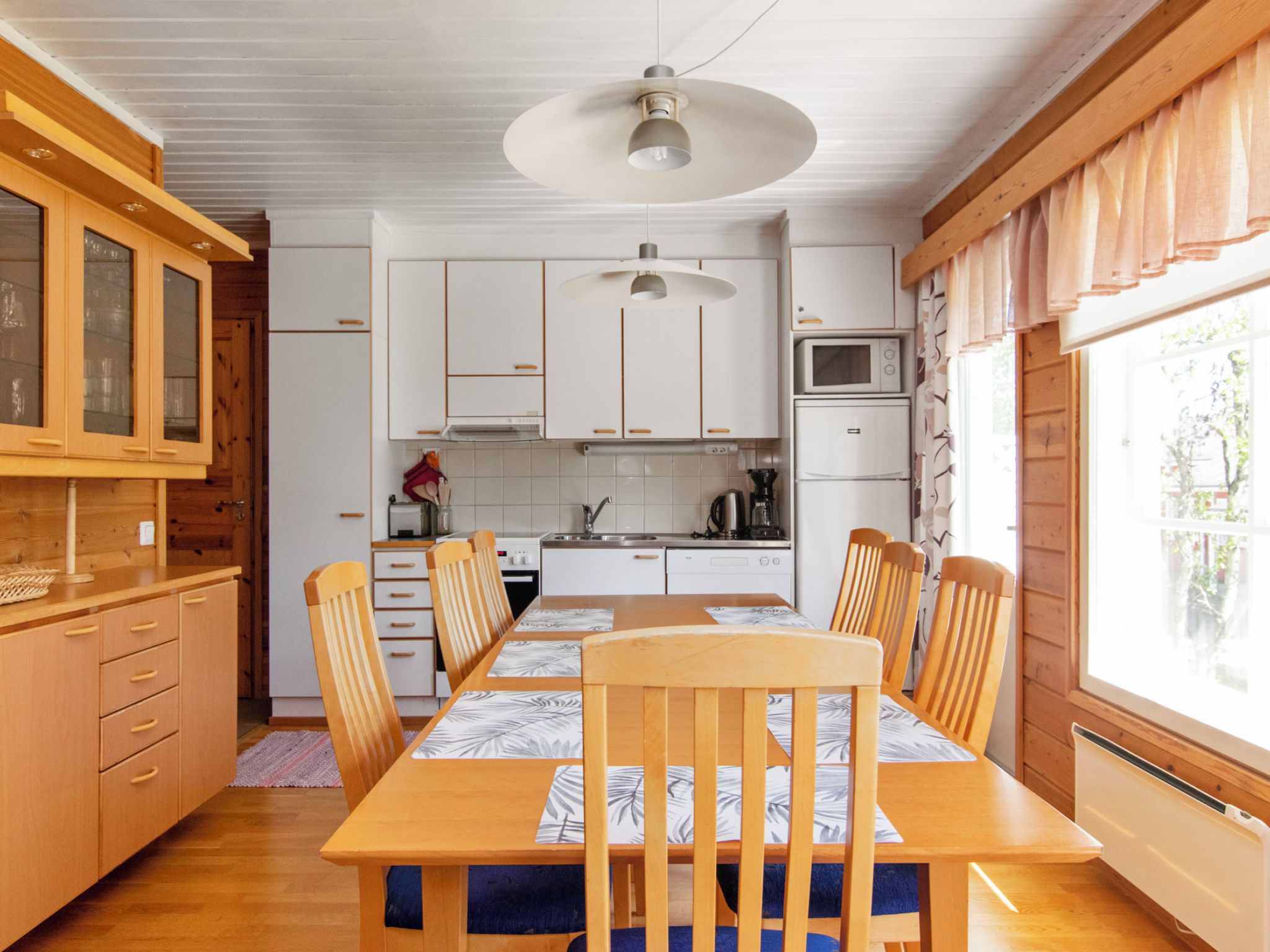Una cocina compacta con armarios blancos, una mesa de comedor con sillas y un ventanal grande.