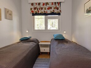 Et værelse med to senge, et lille skrivebord, et vindue og en lampe på væggen.