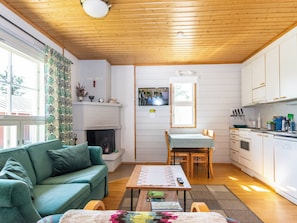 A cozy living room with a sofa, a fireplace, a dining table with chairs, and a kitchen area with cabinets and appliances.
