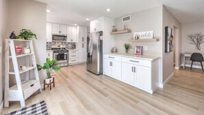 A modern kitchen with white cabinets, stainless steel appliances, and a wooden floor.