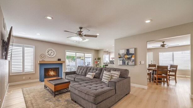 A spacious living room with a sectional sofa, a fireplace, a dining area with a table and chairs, and a ceiling fan.