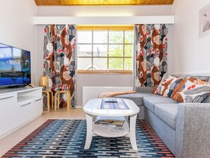 A modern living room with a television, a sofa, a coffee table, and patterned curtains.