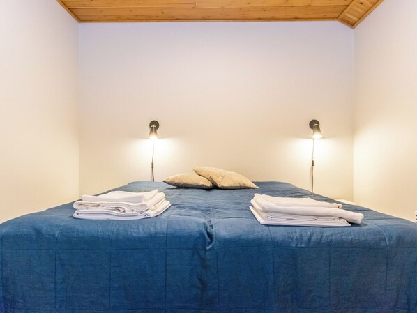 A single bed with a blue bedspread, two pillows, and folded towels on either side. There are two wall-mounted lamps on either side of the bed.