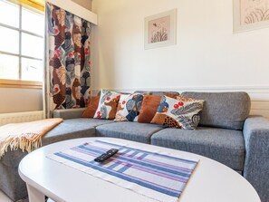 Un salon avec un canapé gris, des coussins à motifs, une table basse blanche et une fenêtre avec des rideaux.