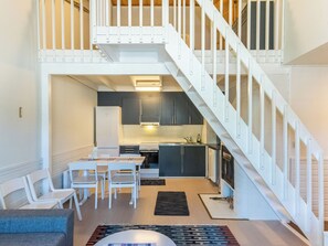 A modern kitchen with dark cabinets, a white staircase, and a dining area with white chairs.