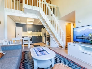 A modern apartment with a living area, a dining space, a kitchen, and a staircase.