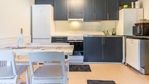 Une cuisine de taille réduite, avec des meubles de couleur sombre, un réfrigérateur blanc, un four à micro-ondes et une cuisinière. On y trouve une table à manger avec des chaises et un petit tapis sur le sol.
