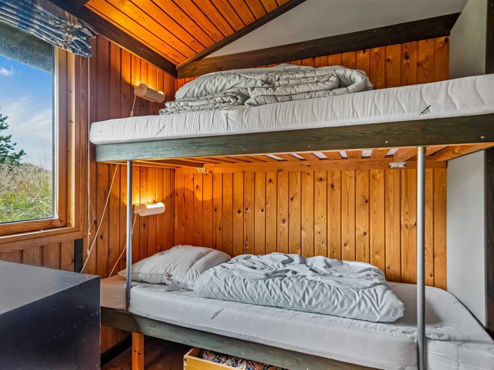 Ein Schlafraum mit Etagenbetten, Holzwänden und einem Fenster mit Blick auf eine natürliche Landschaft.